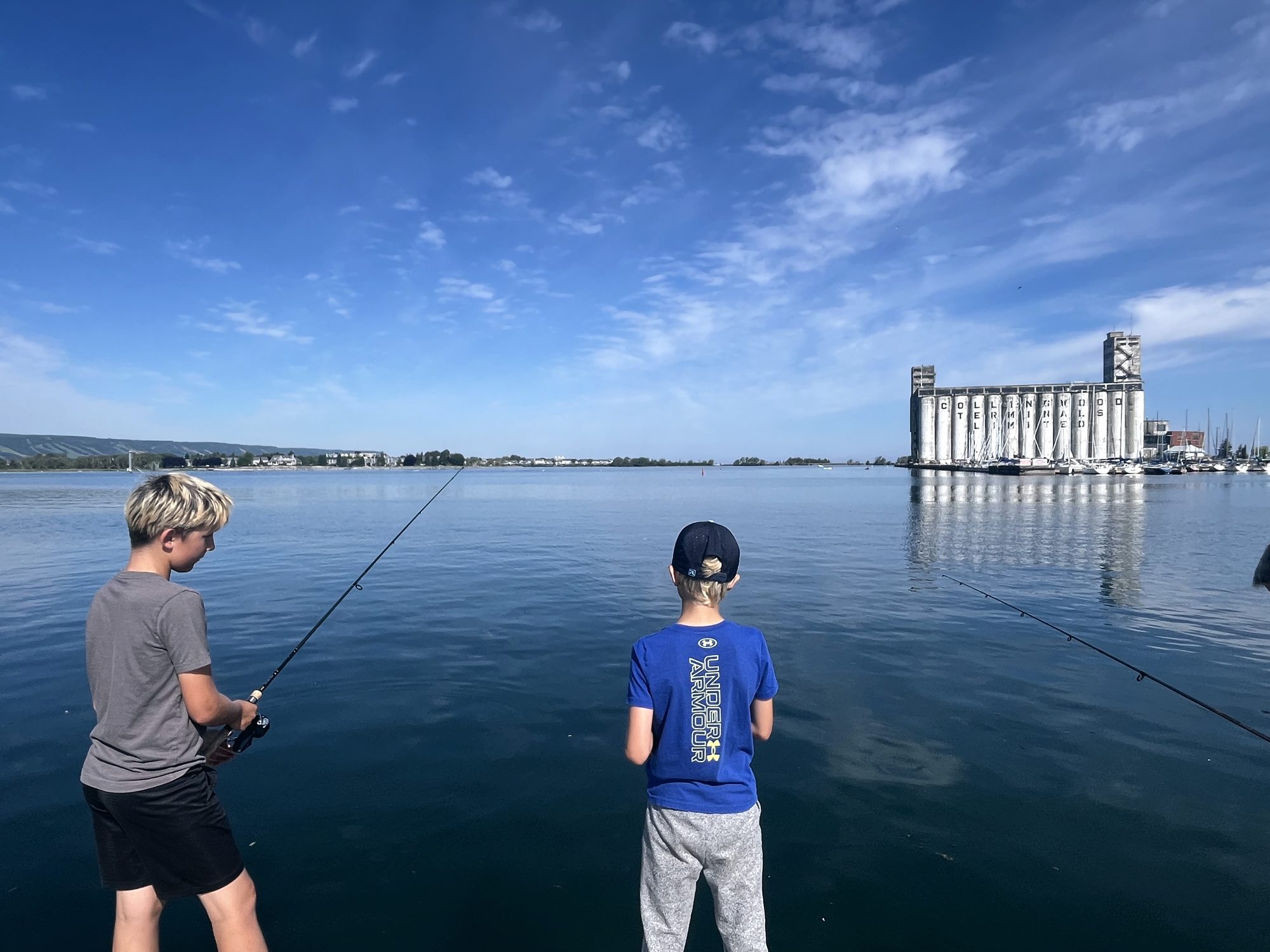 Two boys fishing from the shore, the Collingwood Terminals across the water.